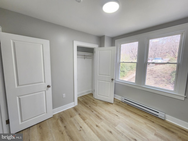 unfurnished bedroom with a baseboard radiator, baseboards, light wood-style flooring, and a closet