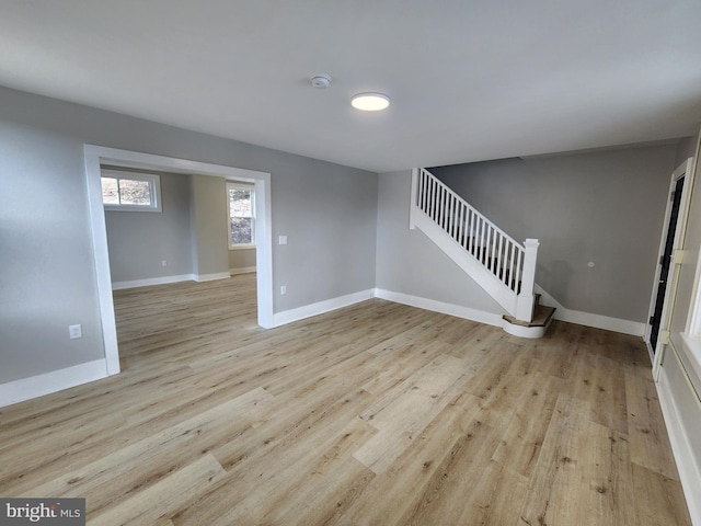 empty room featuring light wood finished floors, baseboards, and stairway