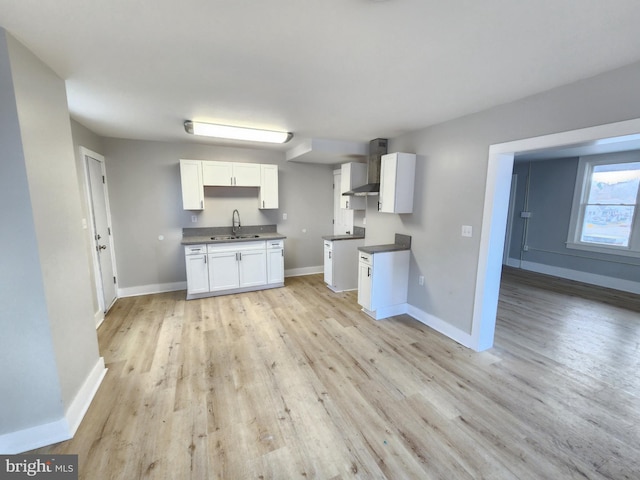 kitchen featuring white cabinets, wall chimney exhaust hood, baseboards, and light wood-style flooring