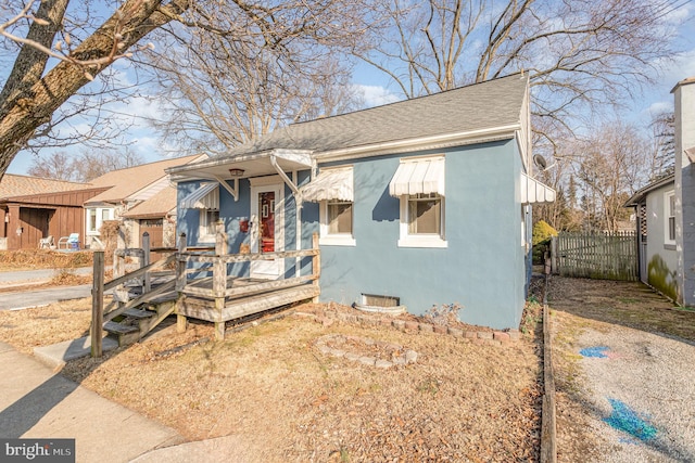 bungalow with roof with shingles, fence, and stucco siding