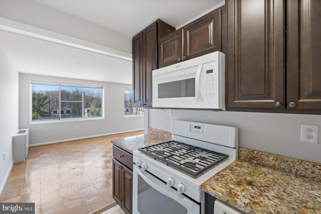 kitchen featuring light stone counters, white appliances, dark brown cabinetry, and baseboards