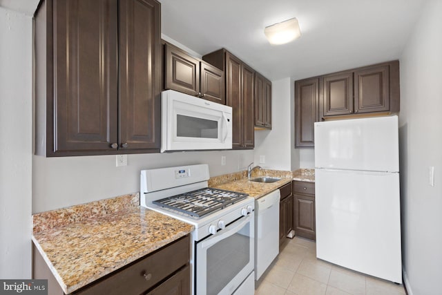 kitchen featuring light tile patterned floors, light stone counters, dark brown cabinetry, white appliances, and a sink