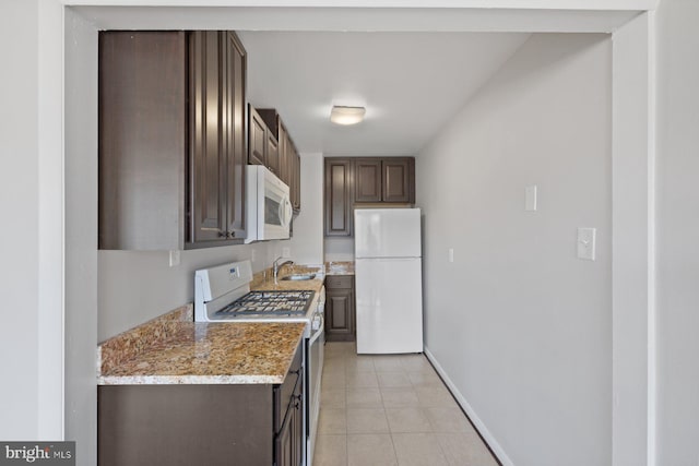 kitchen featuring dark brown cabinetry, white appliances, light tile patterned floors, baseboards, and a sink