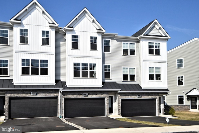 multi unit property with a standing seam roof, stone siding, board and batten siding, an attached garage, and metal roof