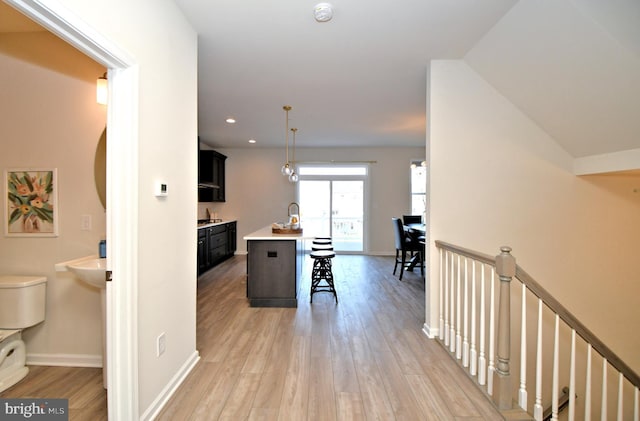 corridor featuring light wood-type flooring, an upstairs landing, and baseboards