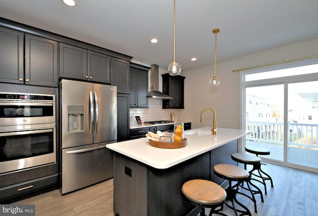 kitchen featuring a kitchen bar, a sink, wall chimney range hood, appliances with stainless steel finishes, and light wood finished floors