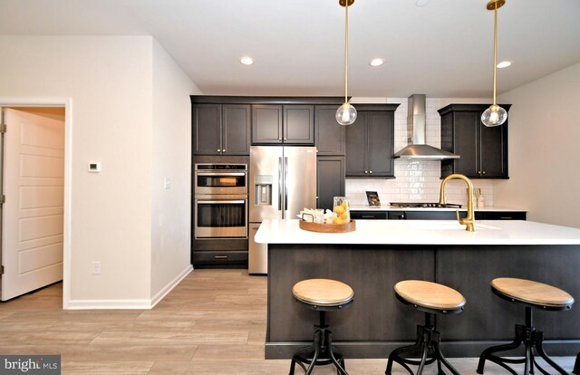 kitchen featuring wall chimney range hood, tasteful backsplash, appliances with stainless steel finishes, a breakfast bar area, and light countertops