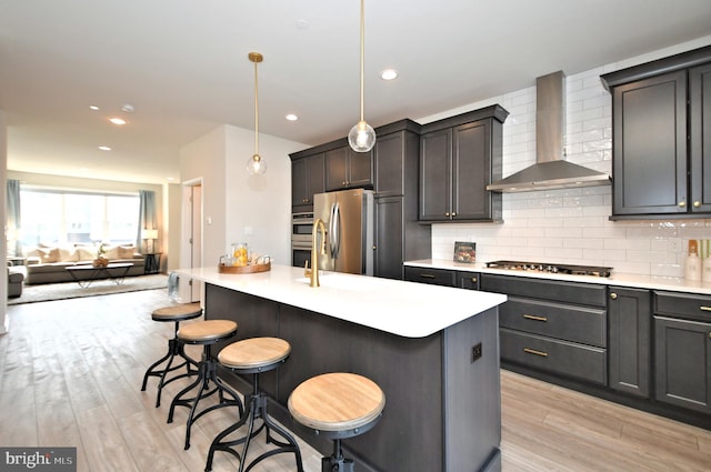 kitchen featuring a kitchen breakfast bar, wall chimney range hood, backsplash, and stainless steel appliances