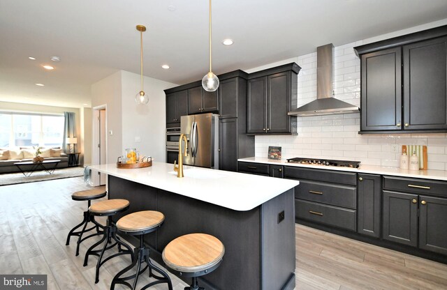 kitchen with a sink, backsplash, appliances with stainless steel finishes, wall chimney exhaust hood, and light countertops