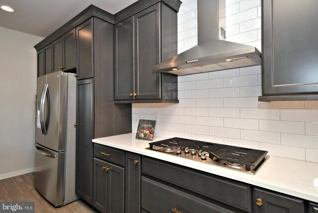 kitchen with wall chimney range hood, stainless steel appliances, light wood-style floors, light countertops, and decorative backsplash