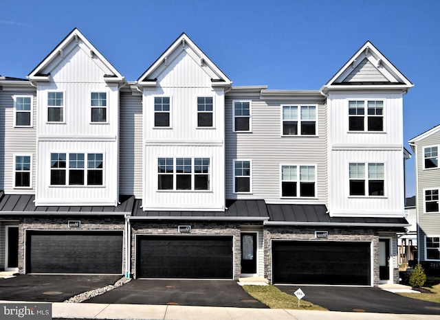 townhome / multi-family property featuring driveway, a standing seam roof, a garage, board and batten siding, and metal roof