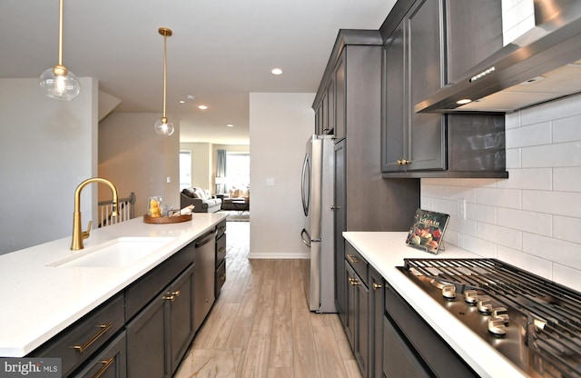 kitchen with appliances with stainless steel finishes, light countertops, wall chimney range hood, and a sink