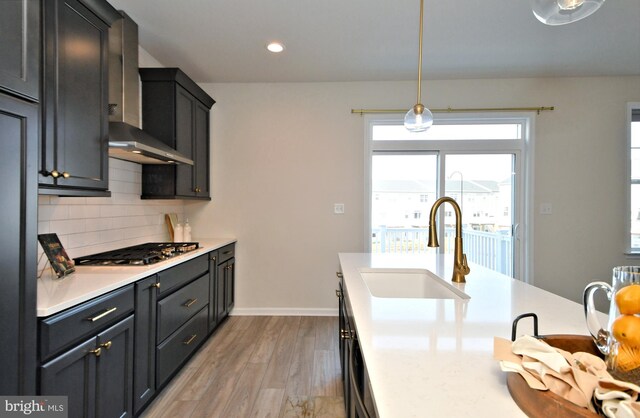 kitchen with stainless steel gas cooktop, light wood-style flooring, a sink, light countertops, and tasteful backsplash