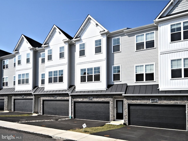 townhome / multi-family property with a residential view, metal roof, stone siding, an attached garage, and a standing seam roof