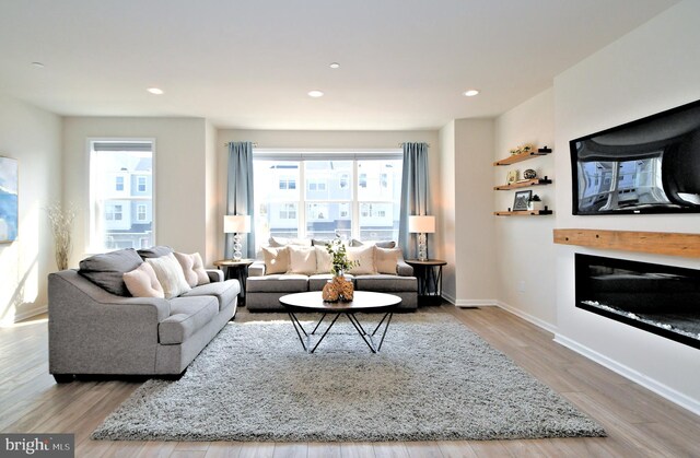 living area with a glass covered fireplace, recessed lighting, wood finished floors, and baseboards