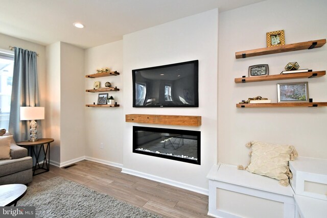 living room featuring visible vents, baseboards, recessed lighting, wood finished floors, and a glass covered fireplace