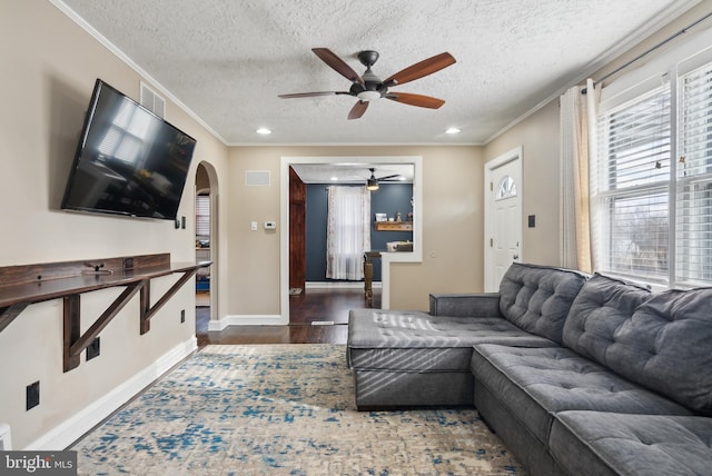 living room with baseboards, arched walkways, ornamental molding, wood finished floors, and a textured ceiling