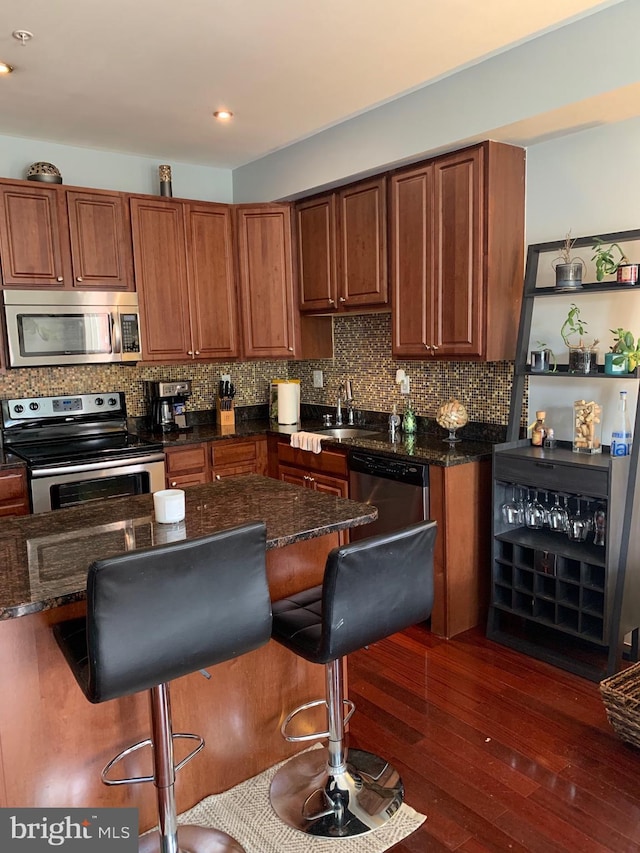 kitchen with a breakfast bar, appliances with stainless steel finishes, decorative backsplash, and dark wood-style flooring