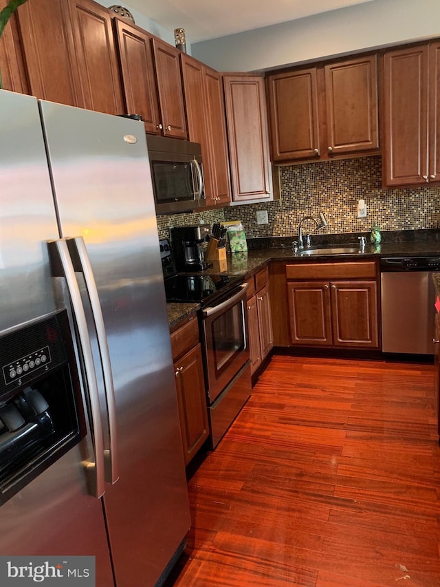 kitchen with stainless steel appliances, tasteful backsplash, a sink, and dark wood finished floors