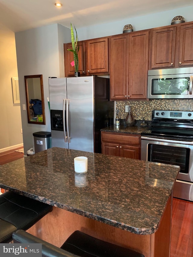 kitchen featuring dark stone counters, a breakfast bar, dark wood-type flooring, stainless steel appliances, and backsplash