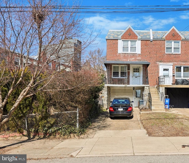 view of property with driveway, stairway, an attached garage, fence, and brick siding