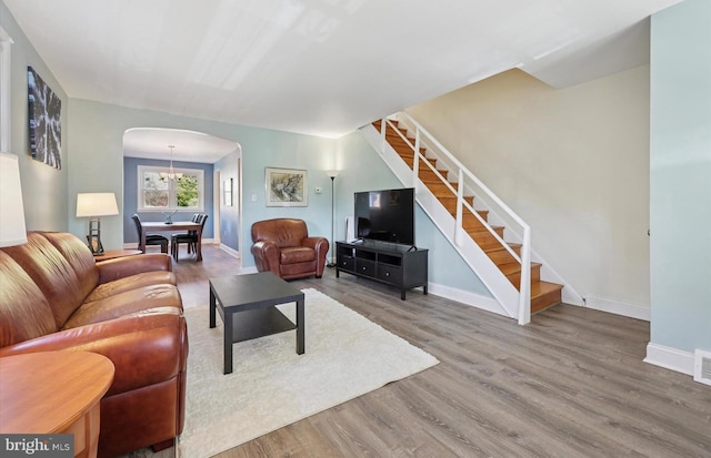 living room with a chandelier, arched walkways, stairway, and wood finished floors