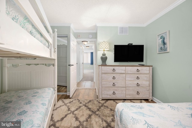 bedroom with crown molding, visible vents, a textured ceiling, wood finished floors, and baseboards