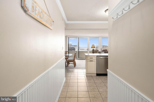 corridor featuring light tile patterned floors, ornamental molding, a textured ceiling, and wainscoting