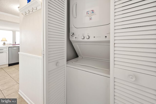 laundry area featuring light tile patterned flooring, a wainscoted wall, stacked washer and dryer, laundry area, and ornamental molding