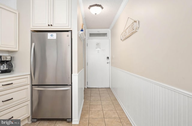 kitchen featuring light tile patterned floors, a textured ceiling, wainscoting, freestanding refrigerator, and crown molding