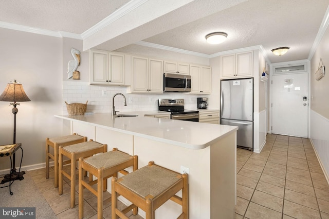 kitchen featuring a peninsula, appliances with stainless steel finishes, a sink, and ornamental molding