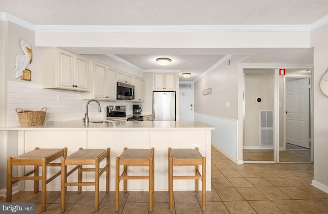 kitchen with appliances with stainless steel finishes, a breakfast bar, a peninsula, crown molding, and a sink