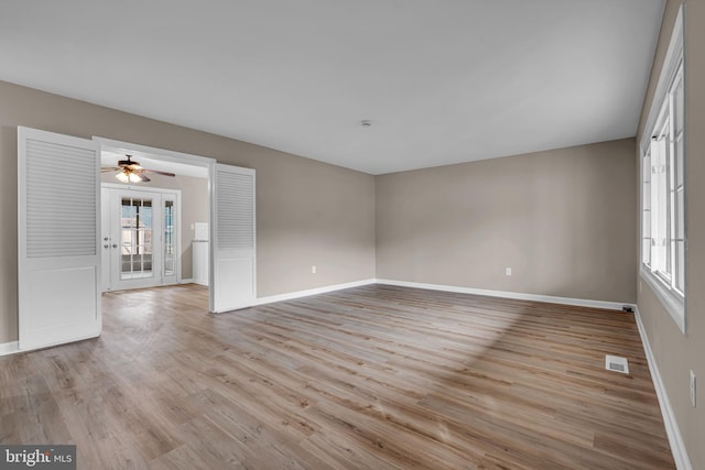 empty room with light wood finished floors, visible vents, and baseboards