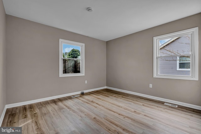 spare room with wood finished floors, visible vents, and baseboards