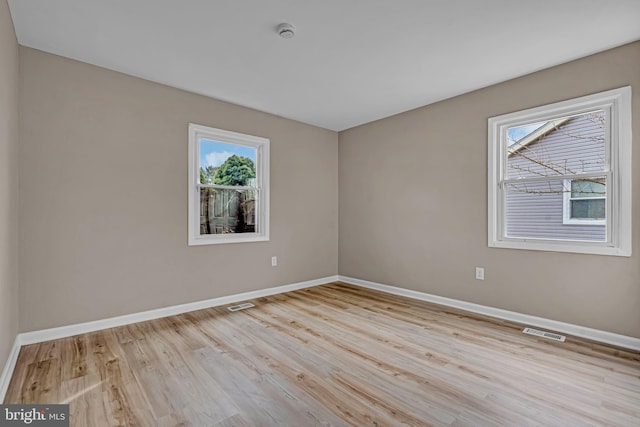 empty room featuring wood finished floors, visible vents, and baseboards