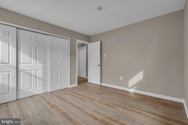 unfurnished bedroom featuring visible vents, a closet, baseboards, and wood finished floors