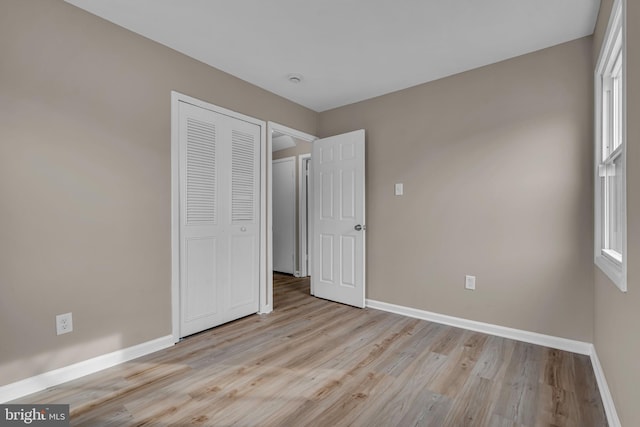 unfurnished bedroom featuring light wood-style floors, baseboards, and a closet