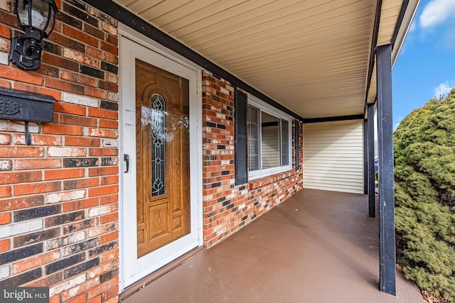 doorway to property featuring a porch and brick siding