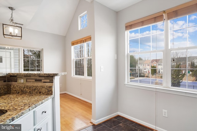 kitchen with white cabinetry, vaulted ceiling, baseboards, and light stone countertops