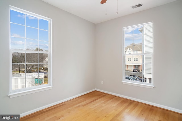 empty room with wood finished floors, visible vents, and baseboards