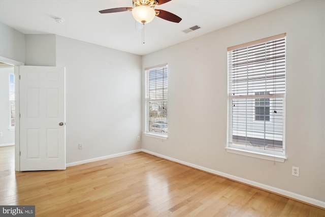 spare room with a ceiling fan, wood finished floors, visible vents, and baseboards