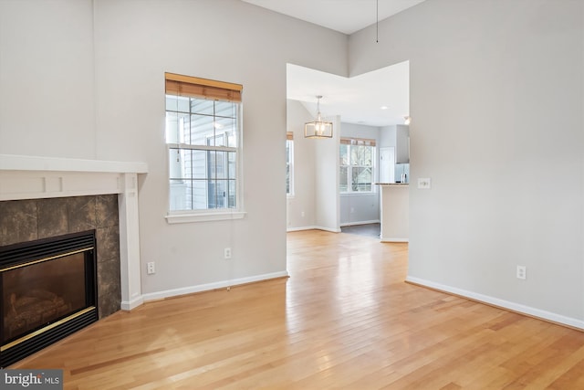 unfurnished living room featuring a tile fireplace, baseboards, and light wood finished floors