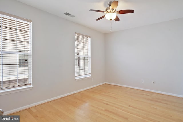 empty room featuring a ceiling fan, wood finished floors, visible vents, and baseboards