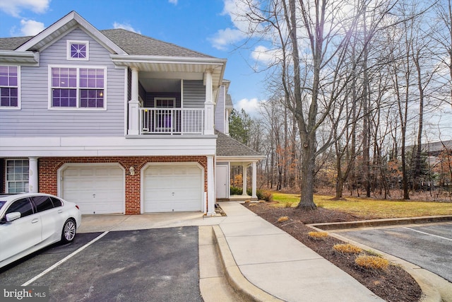 view of front of house featuring a balcony, aphalt driveway, roof with shingles, an attached garage, and brick siding