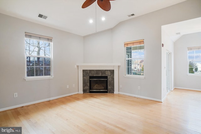 unfurnished living room with light wood-type flooring, lofted ceiling, visible vents, and a tiled fireplace