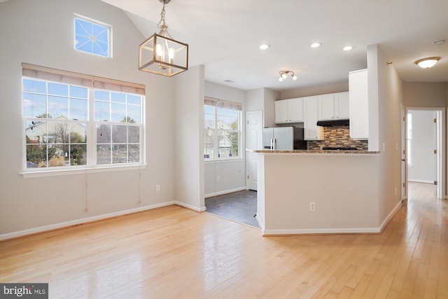 kitchen with white cabinets, decorative backsplash, light wood-style flooring, fridge with ice dispenser, and under cabinet range hood