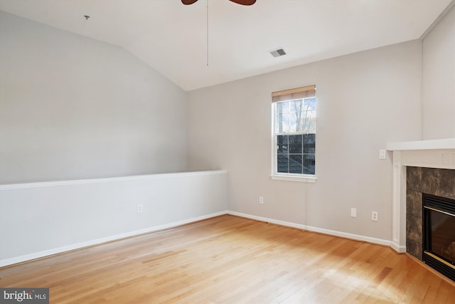 unfurnished living room featuring lofted ceiling, visible vents, a tiled fireplace, ceiling fan, and wood finished floors