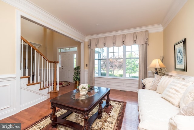 living room with ornamental molding, wood finished floors, stairway, wainscoting, and a decorative wall