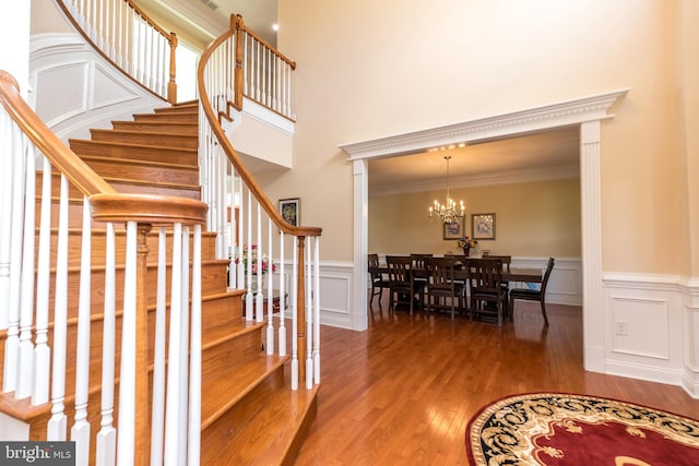 foyer entrance with wood finished floors, an inviting chandelier, ornamental molding, stairs, and a decorative wall