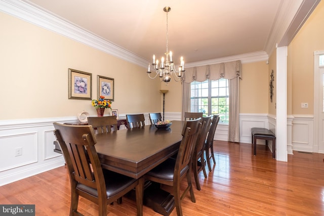 dining room featuring crown molding, light wood-style flooring, a notable chandelier, and a wainscoted wall